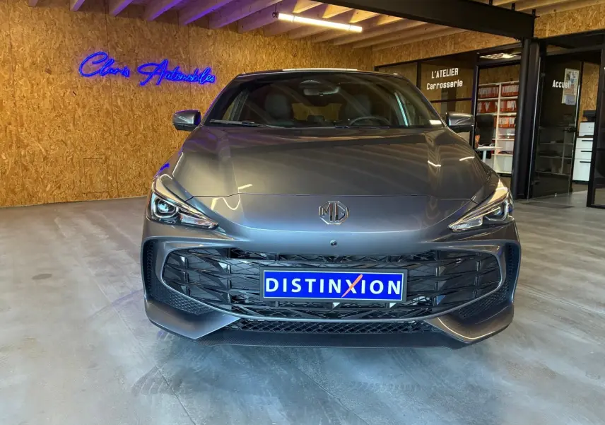 Vue de face d'une MG3 1.5 HYBRID+ 195 LUXURY noire, avec calandre large et phares LED allumés en intérieur showroom.