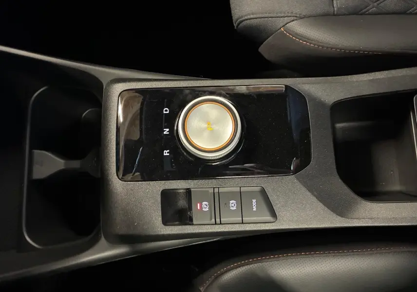 Gros plan sur la console centrale noire du MG3 1.5 HYBRID+ 195 LUXURY avec molette de sélection de vitesse et boutons de frein à main électronique.