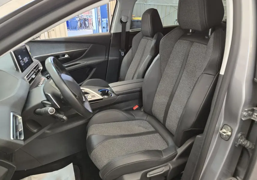 Vue intérieure côté conducteur du Peugeot 5008 gris clair, mettant en valeur les sièges en tissu et cuir ainsi que le tableau de bord digital.