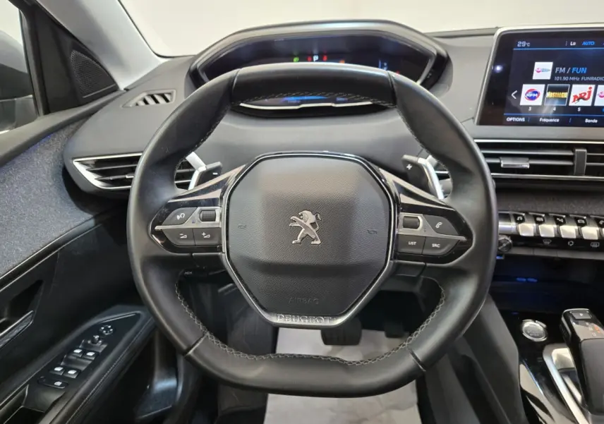 Vue rapprochée du volant cuir noir et du tableau de bord digital d’un Peugeot 5008 gris clair, intérieur moderne et épuré.