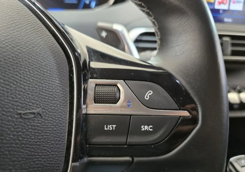 Gros plan sur les commandes noires du volant côté gauche du Peugeot 5008 gris clair, avec boutons LIST et SRC visibles.