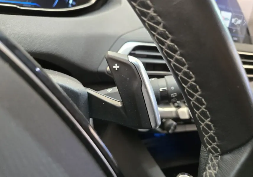 Gros plan sur la palette de changement de vitesse + au volant cuir du Peugeot 5008 gris clair, intérieur moderne et digital.