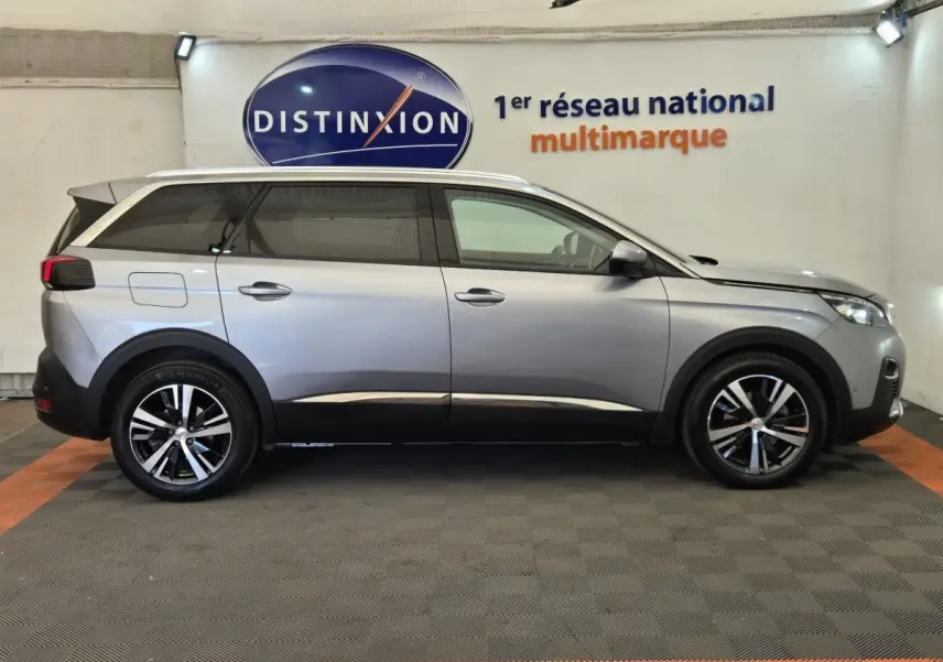 Peugeot 5008 gris clair vue de profil côté gauche, avec jantes alliage et rails de toit chromés visibles.