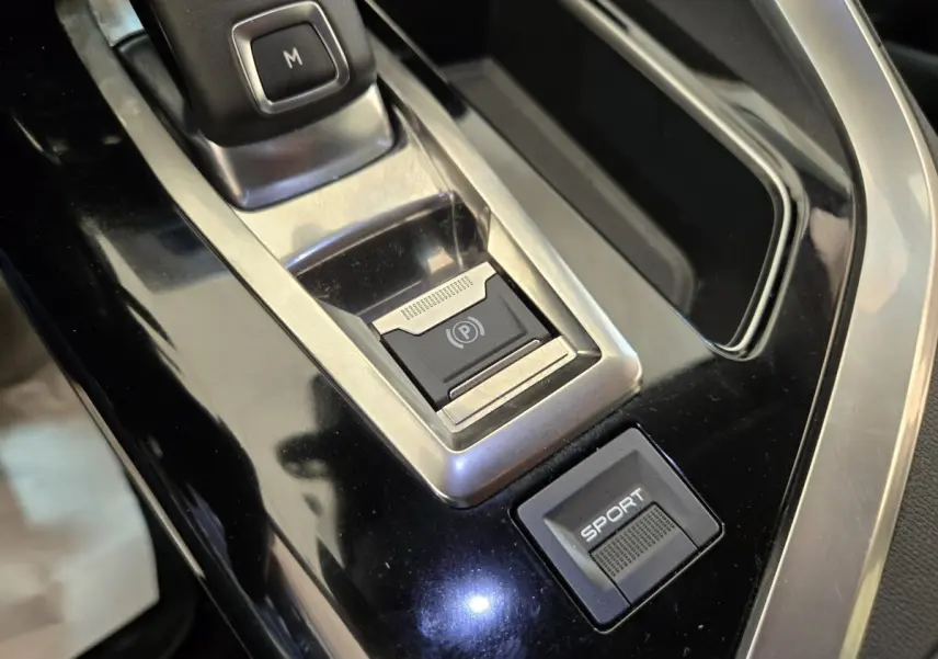 Gros plan sur la console centrale noire brillante du Peugeot 5008 avec bouton frein électrique et mode Sport.