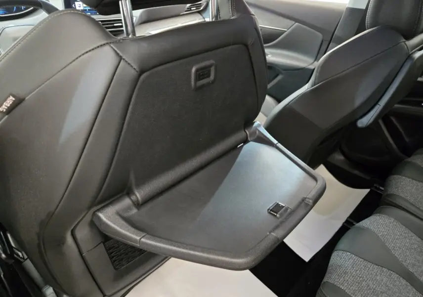 Vue intérieure arrière du Peugeot 5008 gris clair, tablette rabattable sur le dossier du siège avant droit visible.
