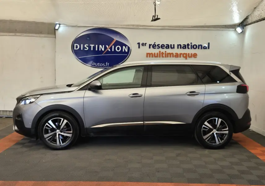Peugeot 5008 gris clair vue de profil côté gauche, avec jantes alliage et toit chromé en intérieur showroom.