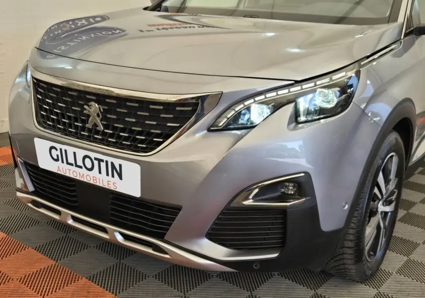 Vue 3/4 avant droit d’un Peugeot 5008 gris clair avec calandre chromée et phares LED allumés.