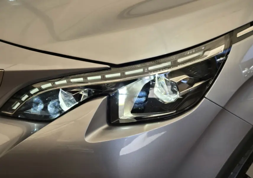 Gros plan sur le phare avant droit du Peugeot 5008 gris clair, mettant en valeur ses LED distinctives et lignes modernes.
