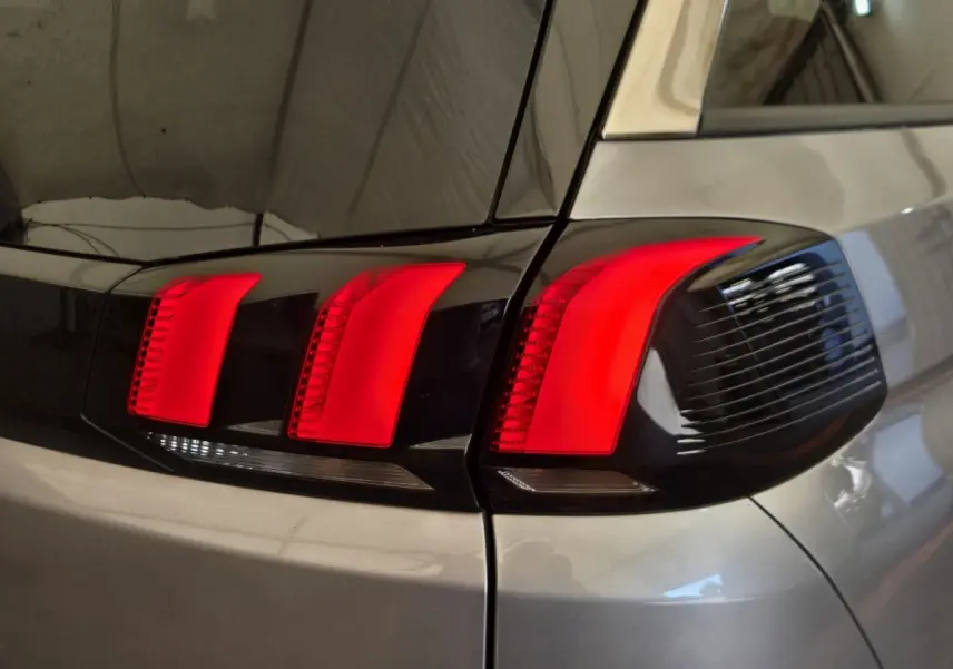 Gros plan sur le feu arrière droit rouge vif d’un Peugeot 5008 gris clair, soulignant ses lignes modernes.