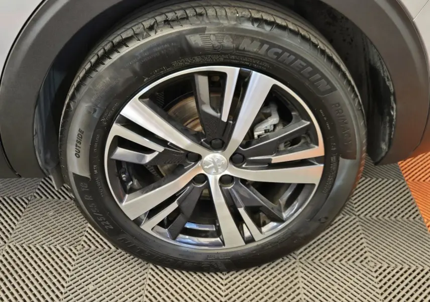 Gros plan sur la roue avant droite du Peugeot 5008 gris clair, mettant en valeur la jante alliage bicolore et le pneu Michelin.