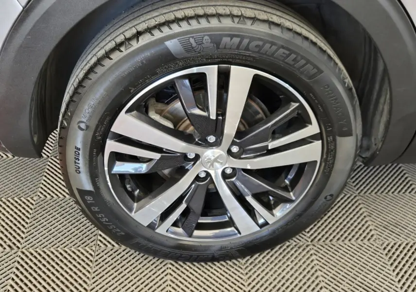 Gros plan sur la roue avant droite du Peugeot 5008 gris clair, avec jante alliage bicolore et pneu Michelin.