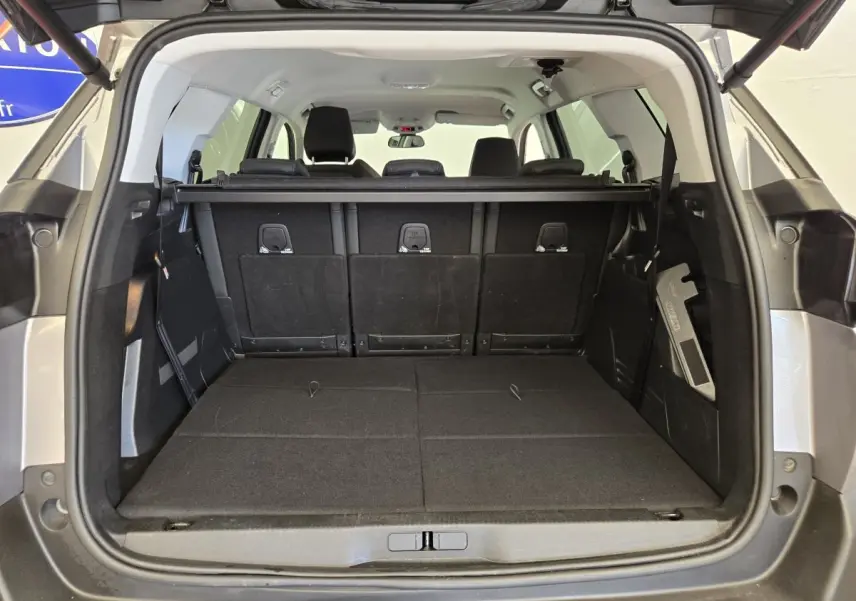 Coffre ouvert vu de l'arrière d'un Peugeot 5008 gris clair avec banquette arrière partiellement rabattue.