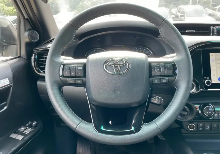 Vue intérieure centrée sur le volant noir du Toyota Hilux 4x4 blanc 2025, avec commandes intégrées et tableau de bord visible.