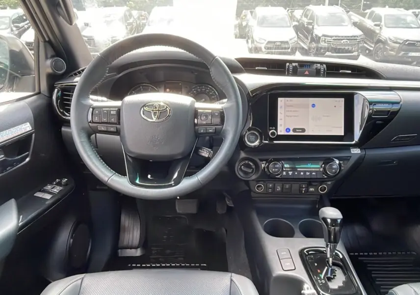 Intérieur du Toyota Hilux 2025 blanc, vue du poste de conduite avec volant multifonction et écran tactile central.