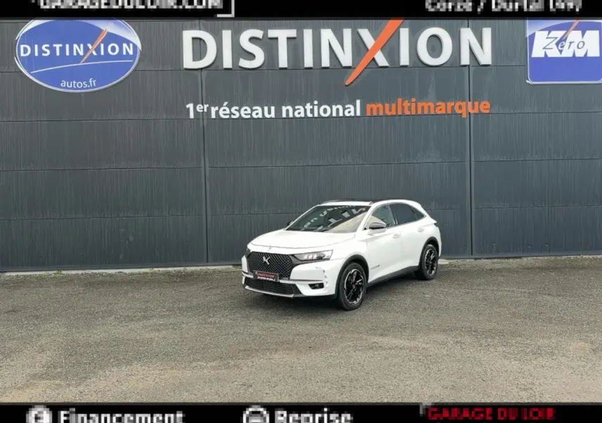 DS7 Crossback blanc en 3/4 avant droit, avec calandre noire et jantes noires, devant un mur gris marqué Distinxion