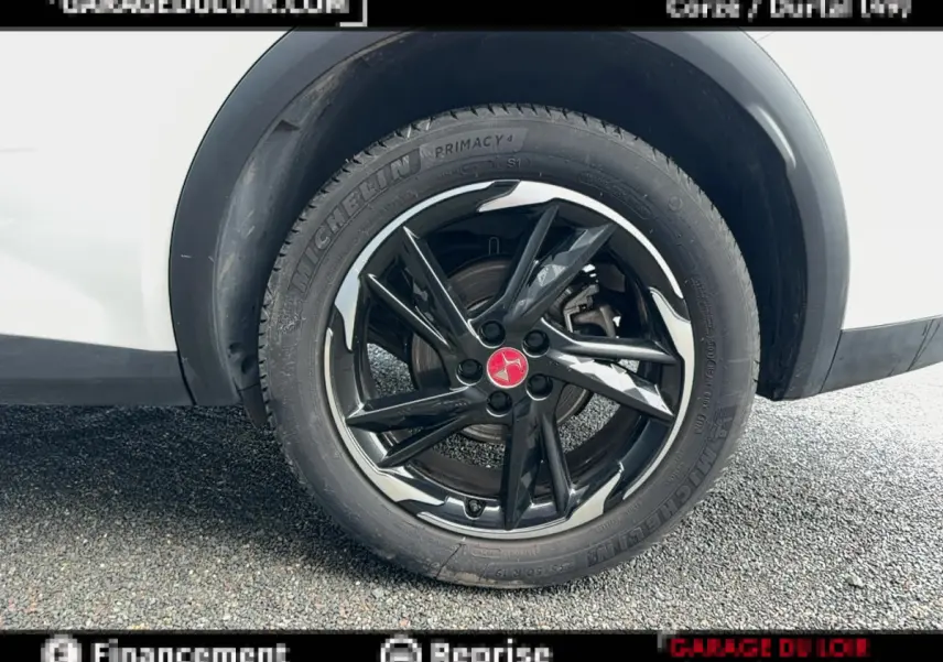 Gros plan sur la roue arrière droite avec jante noire brillante et logo rouge sur DS7 Crossback blanc.