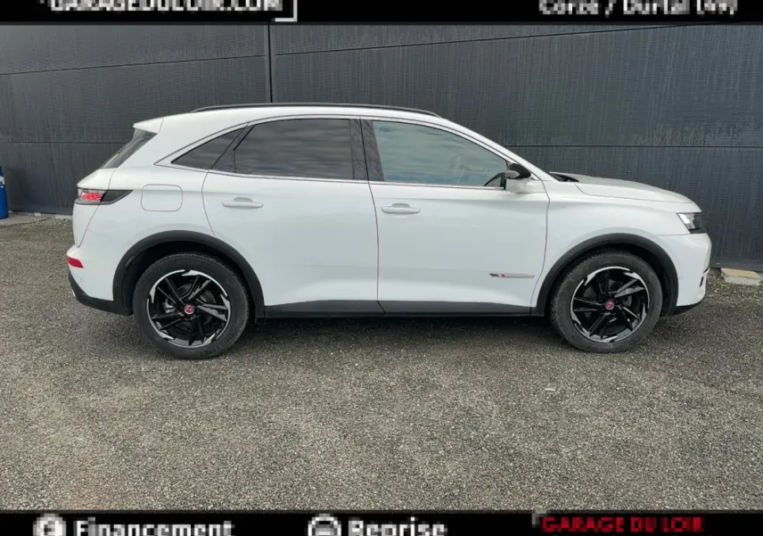 Vue de profil côté gauche d'un DS7 Crossback blanc avec jantes noires et vitres teintées, sur fond gris urbain.