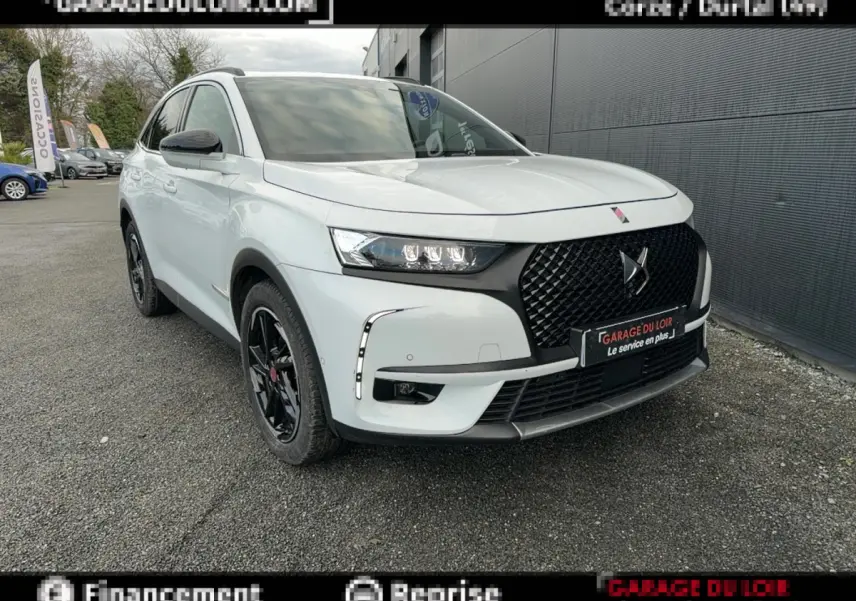 Vue 3/4 avant droite du DS7 Crossback blanc avec calandre noire et jantes noires, stationné devant un mur gris.