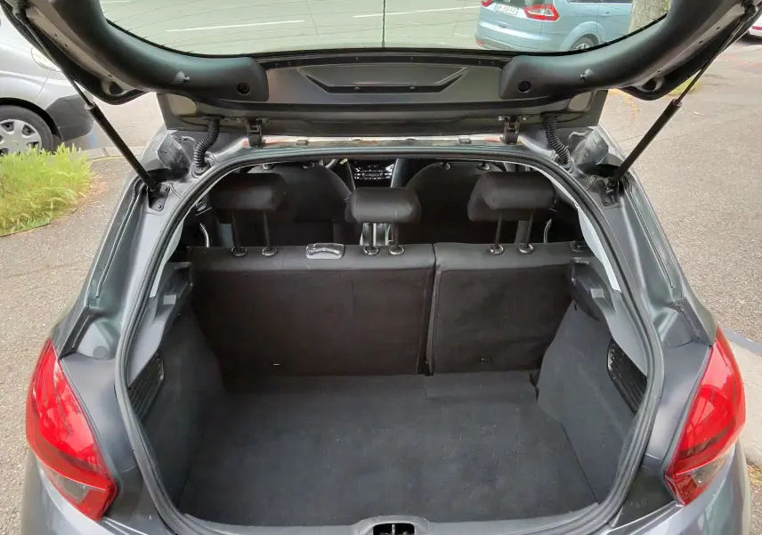 Vue arrière ouverte du coffre d'une Peugeot 208 gris foncé métal, montrant l'intérieur vide et les sièges arrière.