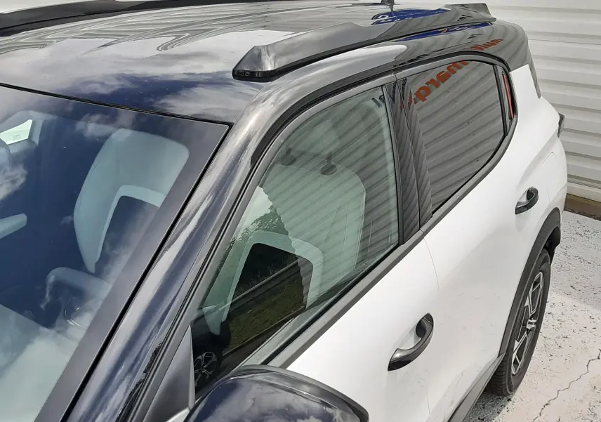 Vue rapprochée côté gauche d’un Citroën C3 Aircross blanc banquise avec toit et rétroviseur noir brillant.