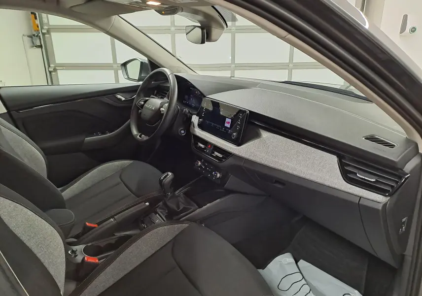 Vue intérieure côté conducteur du Skoda Kamiq 2025, tableau de bord moderne avec écran tactile et sellerie bicolore gris et noir.