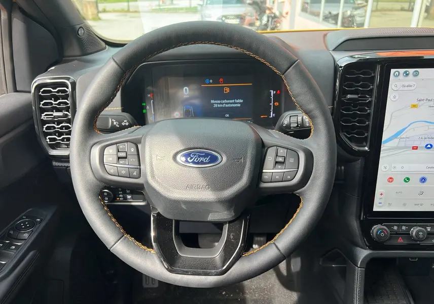 Vue rapprochée du volant noir avec surpiqûres orange du Ford Ranger 2025, affichage numérique et écran tactile de navigation.