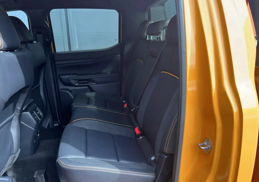 Vue intérieure côté droit sur les sièges arrière noirs avec surpiqûres orange du Ford Ranger Cyber orange 2025 Wildtrak.