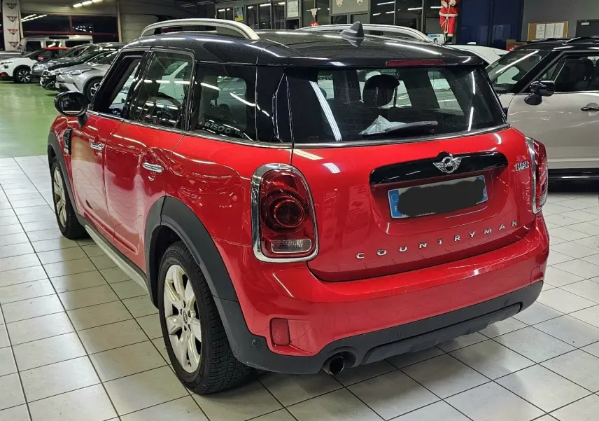 Vue 3/4 arrière droite d'une MINI Cooper Countryman rouge avec toit noir, en intérieur sur carrelage.