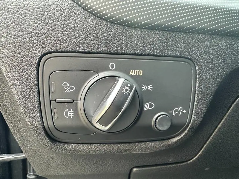 Gros plan sur le sélecteur d'éclairage noir de l'Audi Q2 30 TDI gris Daytona, avec réglage automatique et textures cuir.