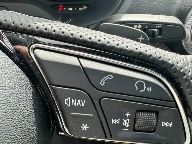 Gros plan sur les commandes vocales et multimédia au volant cuir perforé de l'Audi Q2 30 TDI 2024.