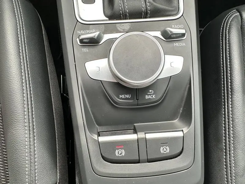 Gros plan sur la molette de commande multimédia et les boutons de frein à main et arrêt auto du moteur, intérieur noir cuir.