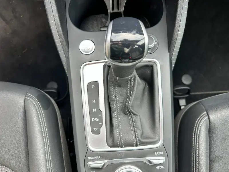 Le levier de vitesses automatique cuir noir de l'Audi Q2 30 TDI S line 2024 vu de dessus entre les sièges avant.
