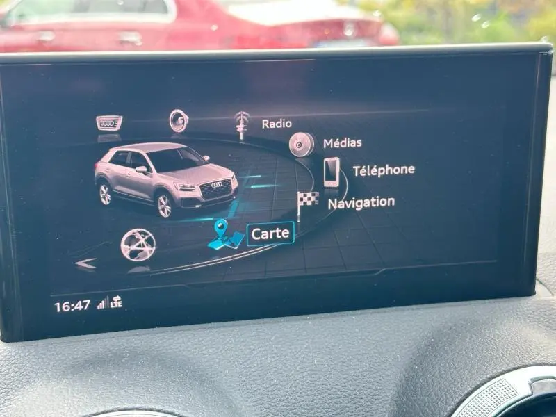 Écran multimédia intérieur affichant un Audi Q2 gris Daytona nacré en vue 3/4 avant avec menu navigation et médias.