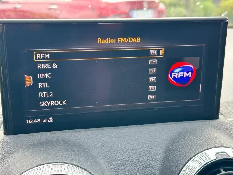 Écran multimédia de l'Audi Q2 30 TDI 2024 affichant la sélection radio FM/DAB avec logo RFM visible.