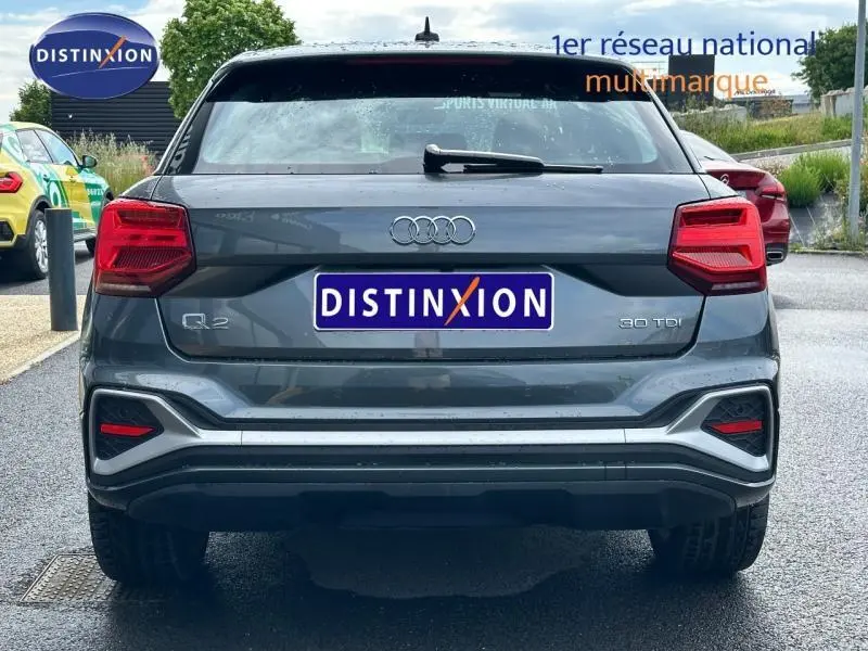 Vue arrière d'un Audi Q2 30 TDI gris Daytona nacré avec feux LED et logo distinctif sur un parking extérieur.