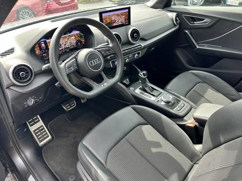 Intérieur noir de l'Audi Q2 30 TDI 2024 vu côté conducteur, volant sport et écran GPS central visible.