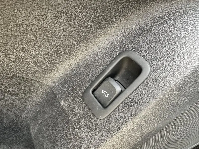 Bouton d'ouverture du coffre en plastique noir sur panneau intérieur texturé d'Audi Q2 gris Daytona nacré 2024
