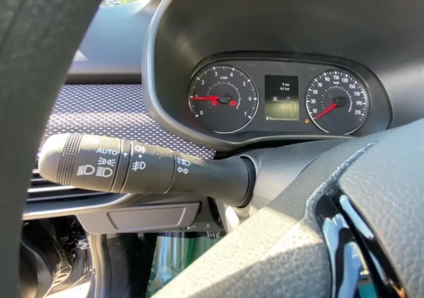 Gros plan sur le combiné d'instruments et la commande des phares à gauche du volant dans le tableau de bord gris de la Dacia Logan 2022.