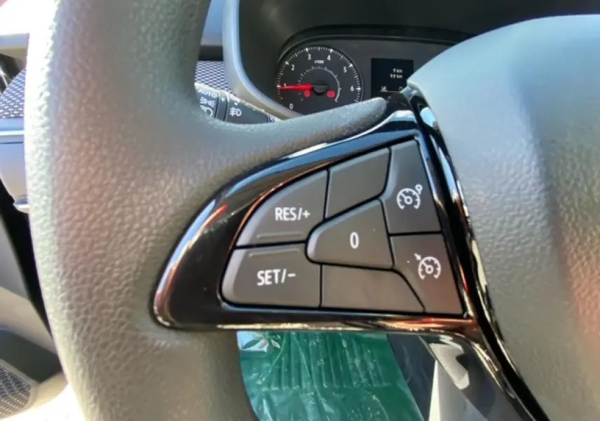 Gros plan sur les commandes du régulateur de vitesse au volant d'une Dacia Logan gris 2022, tableau de bord en arrière-plan.