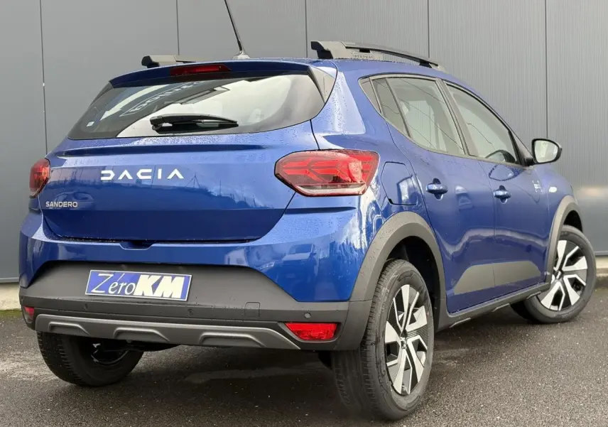 Vue 3/4 arrière droite d'une Dacia Sandero Stepway 2025 bleu Iron avec barres de toit et feux arrière LED en Y.