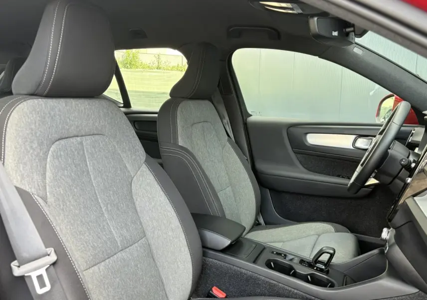 Vue intérieure côté conducteur du Volvo XC40 rouge Fusion, mettant en valeur les sièges gris clair et la console centrale moderne.