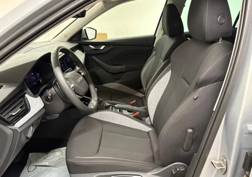 Vue intérieure côté conducteur du Skoda Kamiq gris argent 2025, sièges tissu bicolore noir et gris avec volant multifonction.