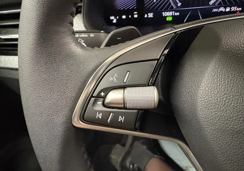 Gros plan sur les commandes gauche du volant noir du Skoda Kamiq gris argent, avec affichage numérique en arrière-plan.