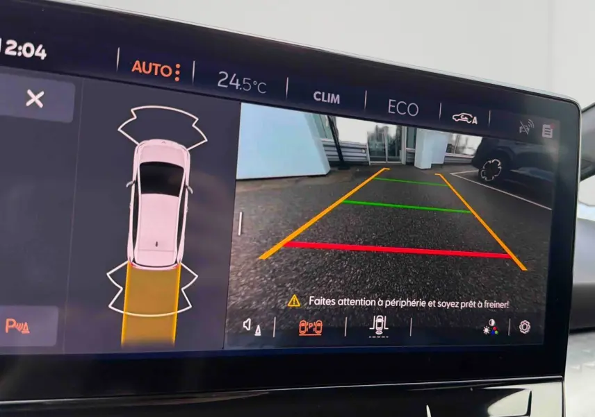Écran tactile du CUPRA Born blanc montrant la caméra de recul avec guidage coloré et alertes de sécurité.