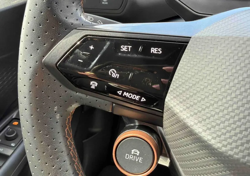Gros plan sur le volant perforé noir de la CUPRA Born 2024 avec commandes de régulateur et bouton Drive orange.