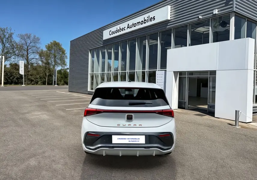 Vue arrière d'une CUPRA Born blanche 2024 avec feux LED et bandeau lumineux Infinite Light, stationnée devant un showroom.
