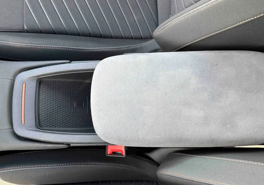 Vue plongeante sur la console centrale du CUPRA Born 2024, avec accoudoir gris clair et sellerie noire à surpiqûres cuivrées.