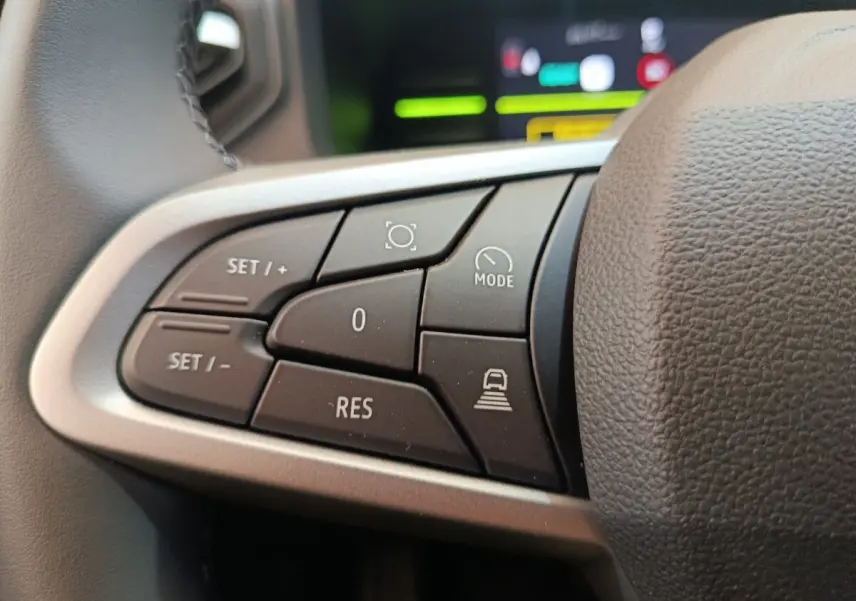 Gros plan sur les commandes au volant du Dacia Duster Journey Hybrid 155, boutons noirs avec marquages blancs.