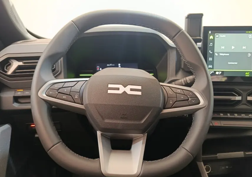 Vue rapprochée du volant noir multifonctions du Dacia Duster Journey Hybrid 155 avec tableau de bord et écran tactile visible.