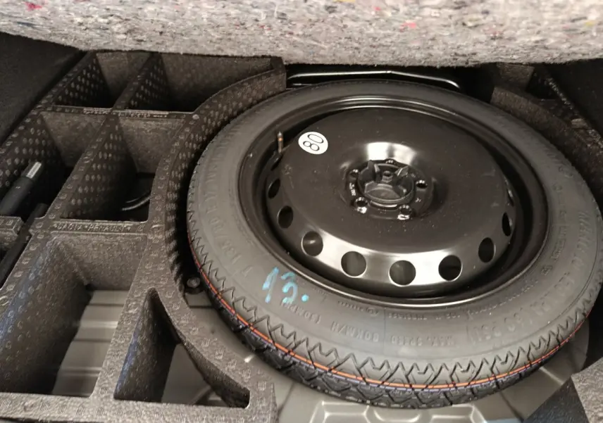 Roue de secours noire dans le coffre compartimenté d'un Dacia Duster noir, vue en plongée rapprochée.